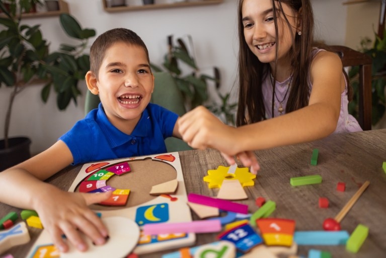 Autism & Inclusion - creating a more welcoming world. A small dark-haired boy with autism plays with his older sister.