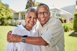 Traveling with a chronic medical condition. Image: senior couple hugging and smiling toward camera while on vacation.