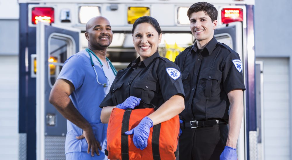 Paramedics and doctor standing at rear of ambulance.  Focus on paramedics (30s, Hispanic).